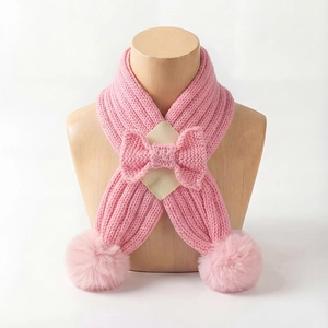 Detailed view of pink knitted baby scarf with ribbed texture, bow, and soft pom-poms