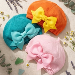 Trois bérets tricotés pour bébé avec de grands nœuds en ruban orange, bleu et rose