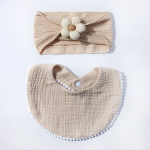 Detail of baby bib and flower headband set in soft beige cotton gauze and knit texture
