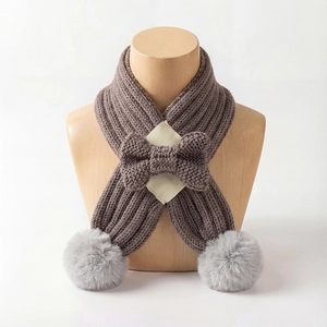 Detail of knitted baby scarf with bow and soft grey pompoms on a wooden display