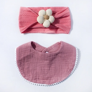 Detail of pink knitted baby headband with fabric flower and matching gauze pom-pom bib