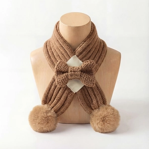 Detail of caramel brown knitted scarf with a bow and soft faux fur pom-poms on a mannequin