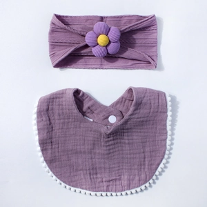 Detail of purple muslin baby bib with pom-pom trim and matching floral headband set