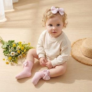 Detail of pink ribbed baby socks with 3D bows and matching headband on wooden floor