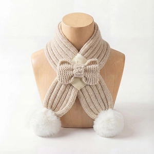 Detail of beige knit baby scarf featuring large white pom-poms and a cute bow tie