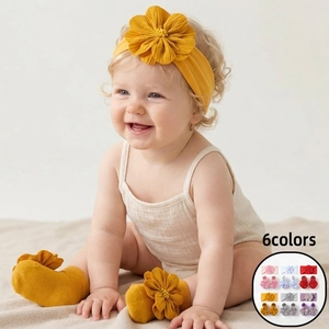 Nahaufnahme von ingwergelbem Baby-Stirnband mit Blumen und Socken auf einem Teppich