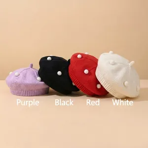 Detail of stacked knitted baby berets in purple, black, red, and white with 3D dots