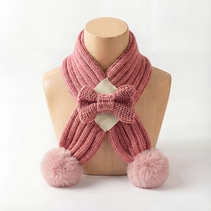 Detail of pink knitted baby scarf featuring a central bow and fluffy pompom charms