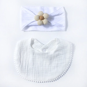 Detailed view of white baby headband with fabric flower and matching pom-pom bib set