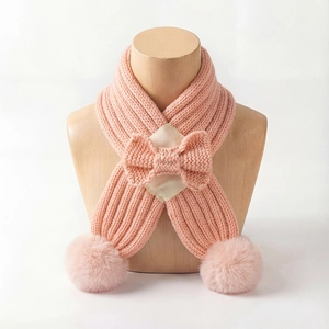 Detail of pink knitted baby scarf with center bow and soft plush pom poms at the ends