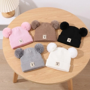 Knit baby beanie with double pom-poms in five colors displayed on a wooden table
