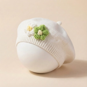 Detail of white knit baby beret featuring handcrafted green and white crochet flowers