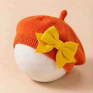 Détail du béret orange tricoté pour bébé avec un grand nœud jaune sur moule blanc