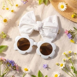 Lunettes de soleil fleur bébé et bandeau en dentelle sur fond de marguerites et paille