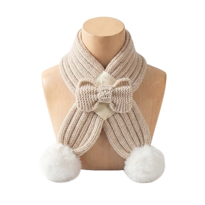 Knitted beige baby scarf with bow tie and white fur pom-poms on wooden display