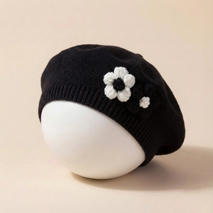 Knitted baby beret hat in black featuring elegant white and black crochet flower decor