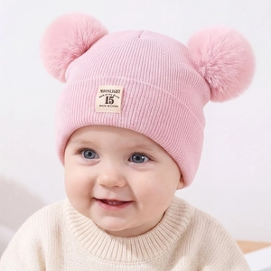 Close-up of pink knitted baby hat featuring two plush pom-poms and vintage woven label