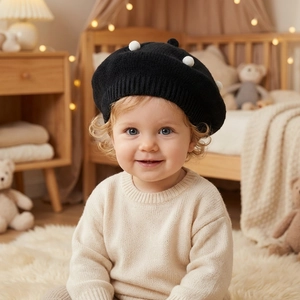 Close-up of knit baby beret in black with white pom-poms on a cozy nursery background