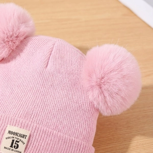 Close-up of pink knit baby hat featuring dual faux fur pom-poms and soft ribbed texture