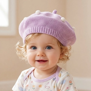 Close-up of purple knitted baby beret with soft white pompom detail and fine texture