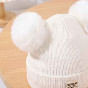 Detail of soft cream knitted baby beanie with two fluffy faux fur pom poms and cloth label