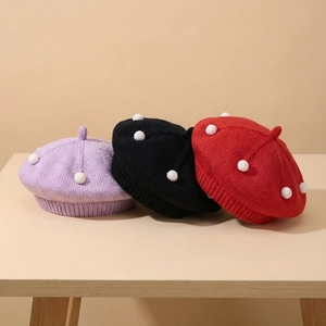 Detail of knitted baby berets in purple, black, and red with white pom-pom accents