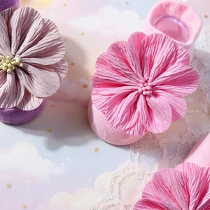 Nahaufnahme von Babysocken mit zarten Satinblumen und Perlen in sanften Pink-Tönen