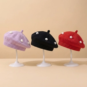 Detailed display of knitted baby berets in purple, black and red with white pom-poms
