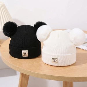 Detail of black and white knitted baby hats with double pom-poms on a wooden table