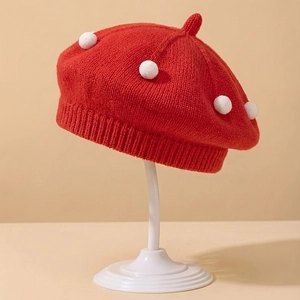 Detail of red knitted baby beret with white pom-poms on a minimalist display stand