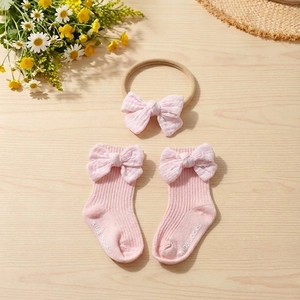 Detailed view of pink bow baby socks and matching headband on a natural wooden background