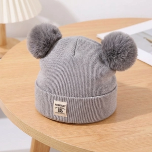 Detailed texture of grey knit baby hat with dual faux fur pom-poms and logo tag