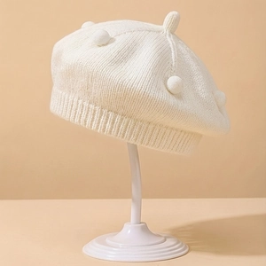 Close-up of cream knit baby beret featuring soft pom-poms and ribbed elastic trim