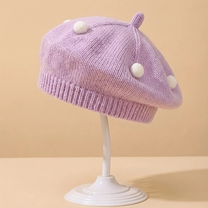 Detail of a lilac knitted baby beret featuring white pom-poms and soft texture