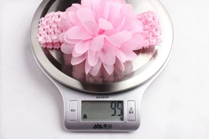 Détail montrant le poids ultra-léger de 9,9g du bandeau bébé fleur en mousseline sur balance