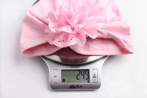Détail montrant le turban rose pour bébé pesant 24,9g sur une balance de cuisine