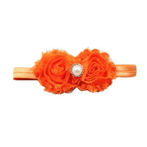 Détail de fleurs en mousseline orange avec perle et strass sur un bandeau pour bébé