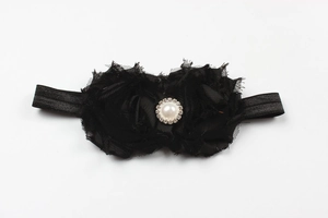 Détail d'un bandeau bébé avec fleur en mousseline noire, perle centrale et strass brillants