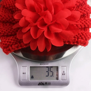 Détail d'un bandeau bébé en maille rouge avec grande fleur posé sur une balance digitale