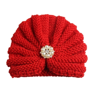 Detailed view of red knitted baby hat featuring pearl flower and rhinestone accents