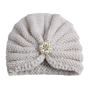 Detailed macro view of cream knitted baby turban hat with elegant pearl and rhinestone flower