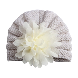 Détail d'un bonnet tricoté pour bébé avec une grande fleur en mousseline sur le dessus