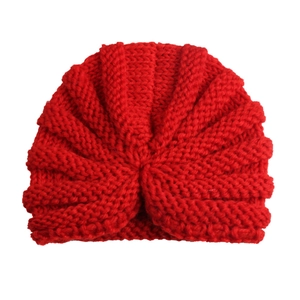 Detail showing the red knitted baby hat's unique turban knot and soft texture