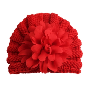 Détail du bonnet en tricot rouge pour bébé orné d'une grande fleur en tissu à plusieurs couches