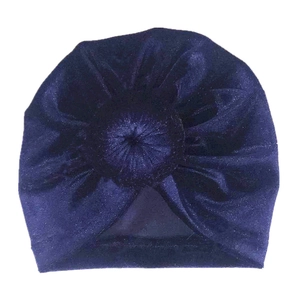 Détail du bonnet turban bébé en velours bleu marine avec un nœud décoratif sur fond blanc