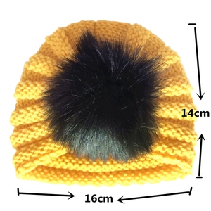 Detailed view of yellow knit baby hat with black faux fur pompom and size dimensions