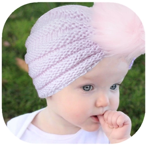 Soft pink baby winter knit hat with large faux fur pompom on infant model outdoor