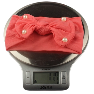 Detail showing a 11.7g soft coral pink nylon baby headband with faux pearls and bow