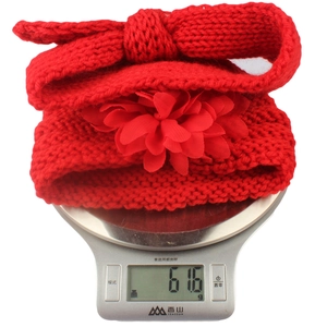 Detail view of a red knitted baby headband with bow and flower weighing 61.6g on a scale
