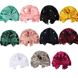 Flat lay of velvet baby turbans featuring pearl bow details in eleven various colors